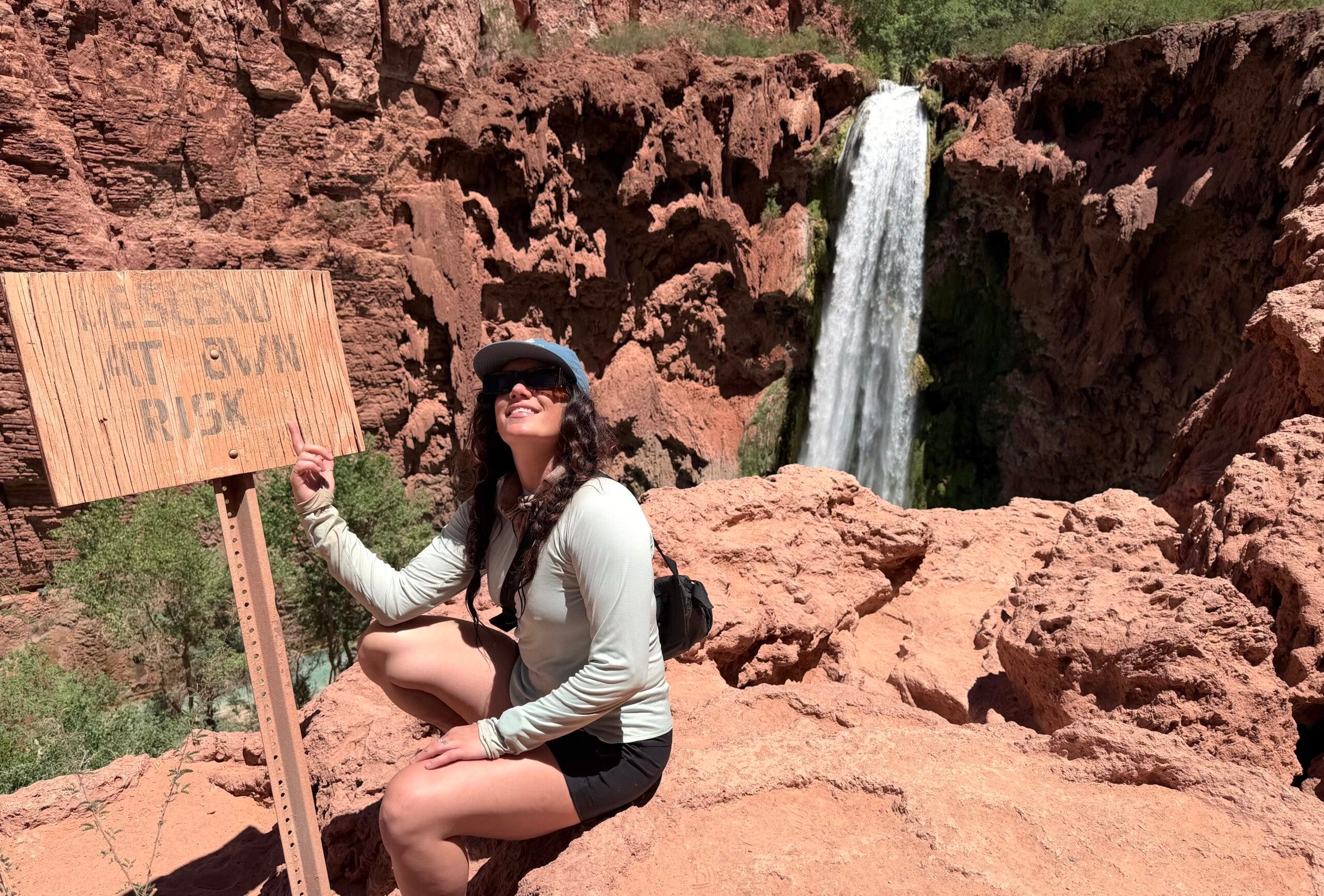 madison dapcevich stands in front of a "descend at your own risk sign" above mooney falls